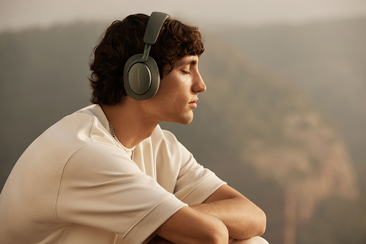Man facing away from the camera has his eyes closed and his arms crossed as he is wearing the Bowers and Wilkins Px7 S2e headphone (Forest Green finish)