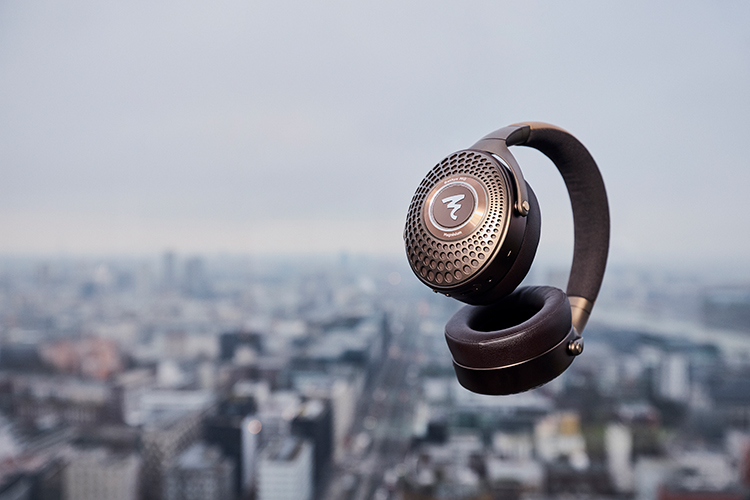 Digital promotional marketing image of the Focal Bathys MG Headphone product model being in air in motion layered over on top of a cityscape background