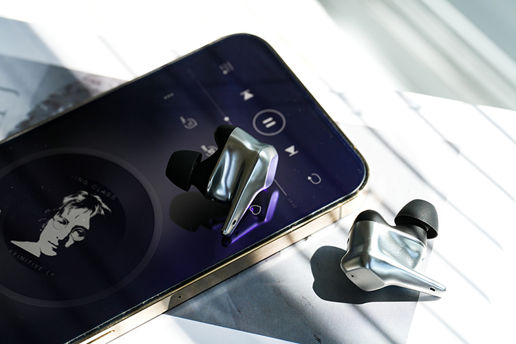 HIFIMAN SVANAR Wireless LE Bluetooth 5.2 Earbud sitting on top of an Apple iPhone model while the other earbud is resting on top of the table surface
