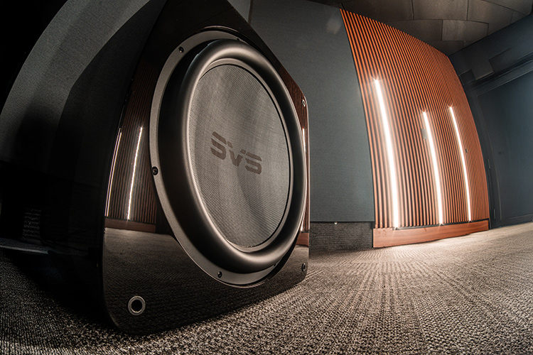 Landscape orientation photograph ground level front angle side view of a high-end home theater cinema room area showcasing the SVS SB17-Ultra R|Evolution subwoofer nearby some bright wall spotlights