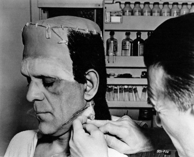 Black and white photograph of Jack Pierce transforming and operating on the Universal Pictures Frankenstein® Monster Character (played by Boris Karloff) Face Close-up Makeup View Black and white photograph of Jack Pierce transforming and operating on the Universal Pictures Frankenstein® Monster Character (played by Boris Karloff) Face Close-up Makeup View
