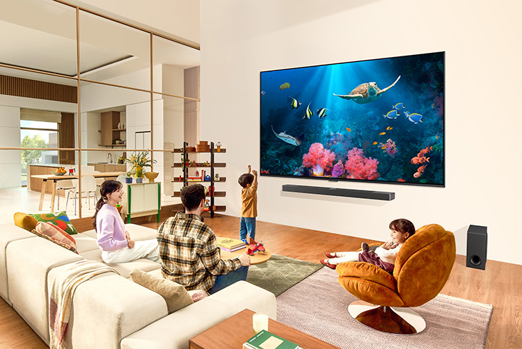 A family of four are seated in the living room area watching the new enhanced picture quality 2024 LG QNED Mini LED TV screen as everyone is happy