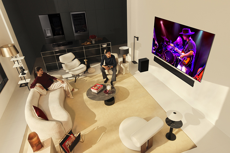 Two happy individuals are seated down in a living room watching a concert on the LG OLED G4 TV model