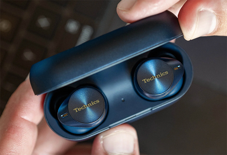 Close-up portrait photograph view of a person's fingers holding the Technics EAH-AZ80 True Wireless Earbuds Midnight Blue Finish as the earbuds are inside their respective open case