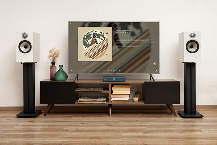 Landscape photograph view of a home theater hi-fi audio living room set-up showcasing the Volumio Rivo Plus streamer product model and other various random assorted product models such as loudspeakers and built-in tabletop stereo speakers while the television screen shows the music track song screen titled Fill or Kill by Frank Musi from the album Spread The Sheets
