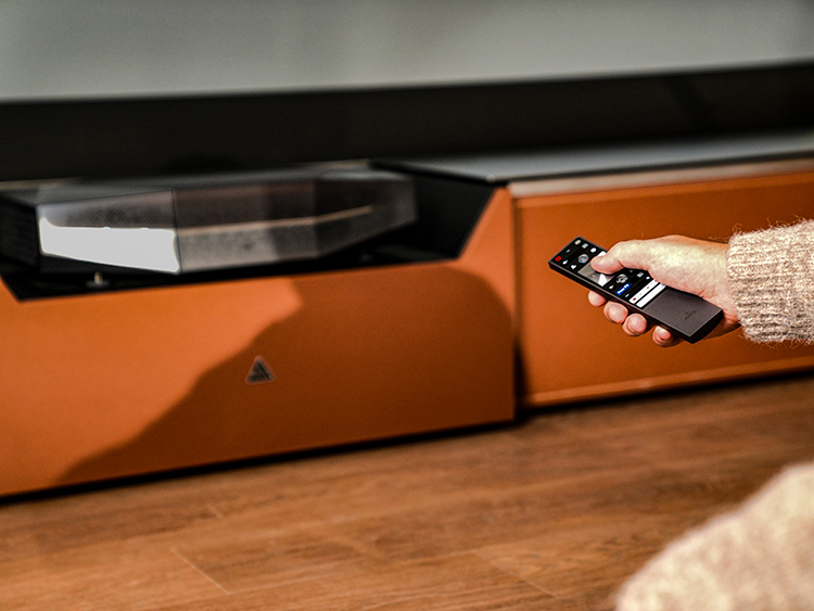 Person's hands using a remote to click on the button to signal the AWOL Vision Aetherion 4K 200-Inch UST Projector