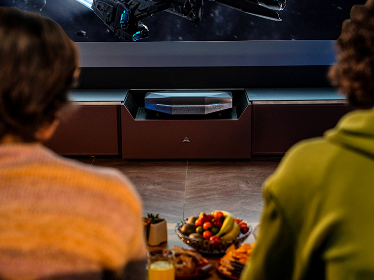 Rear behind back view of two male persons looking at a television which also has the AWOL Vision Aetherion 4K 200-Inch UST Projector situated underneath