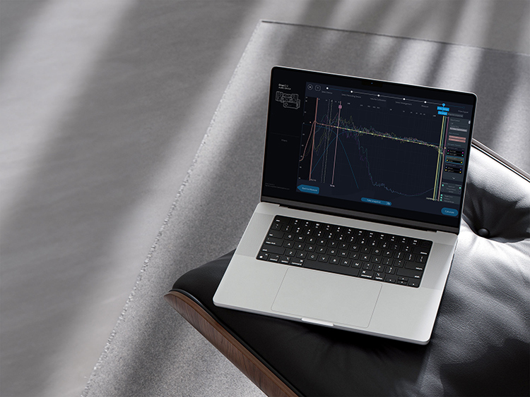A laptop computer screen displaying the Dirac Live software interface, showing a graph of audio frequency response with green and yellow lines, along with numerical data, against a blurred room background