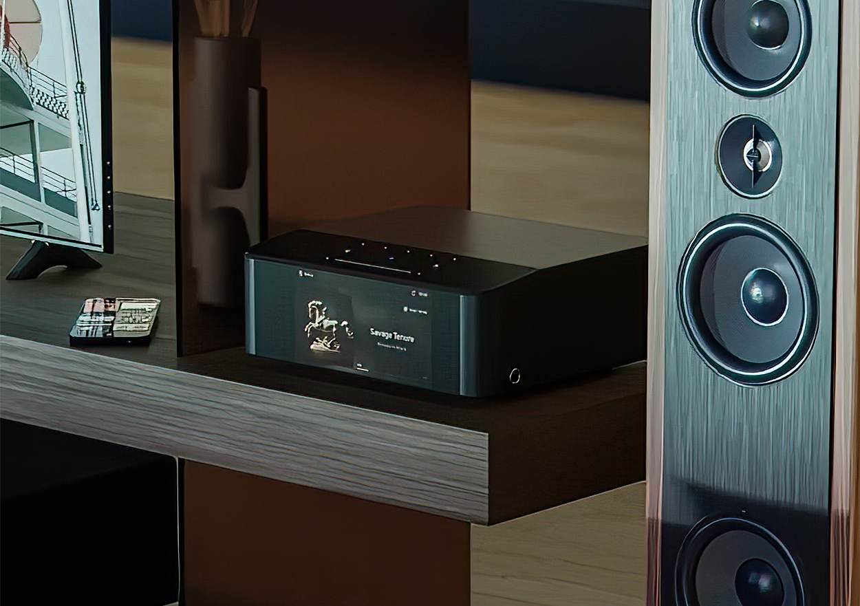 Bluesound Node Icon Music Streamer situated nearby a smartphone, a television, and a floor-standing loudspeaker audio speaker model Bluesound Node Icon Music Streamer situated nearby a smartphone, a television, and a floor-standing loudspeaker audio speaker model