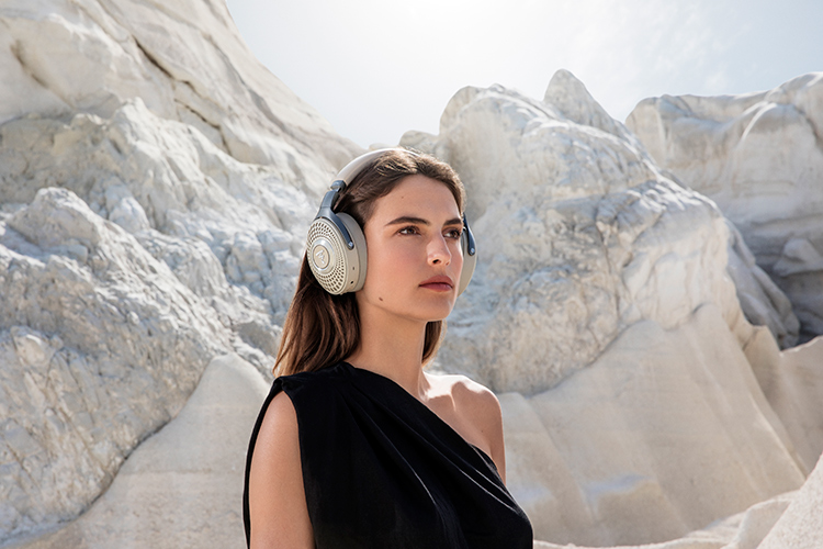 Woman in a black dress looks out into the opposite distance while wearing the Focal Bathys Dune Finish Headphone around her head/ears outside in a desert rock/canyon rock area