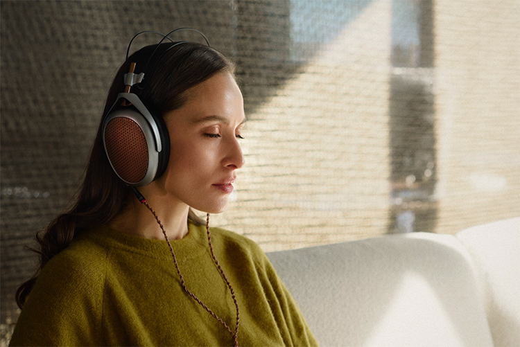 Portrait orientation close-up photograph view of a woman in a dark olive green sweatshirt with her eyes closed as she relaxes while she enjoys listening to her Meze Audio POET planar-magnetic headphone around her ears