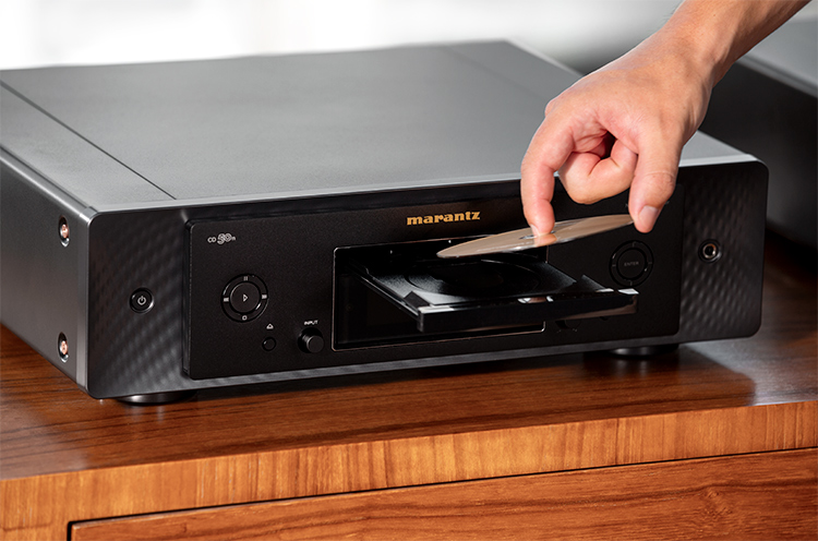 Close-up photograph perspective of a person's hand inserting a CD into the Marantz CD 50n Networked CD Player open tray