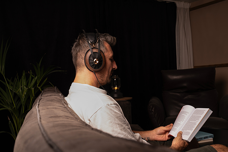 Man wearing Meze Audio 109 Pro Primal Headphone over his head/ears while reading a book in the living room