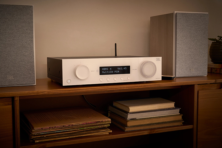 Living room lifestyle close-up landscape photograph view of the JBL MA310 AV Receiver located in between two JBL bookshelf speaker product models on top of a drawer that contains vintage books and music album covers underneath