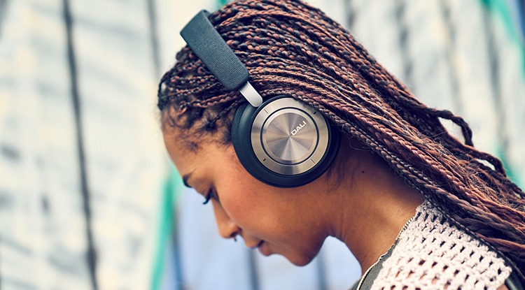 Woman in a braided hairstyle looks down at the ground as she is listening to her DALI IO-8 Headphone Iron Black Finish