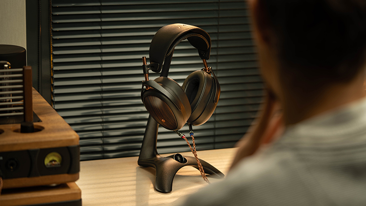 Rear view of a person glancing at a Meze Audio LIRIC 2nd Generation Headphone situated on top of a headphone stand product
