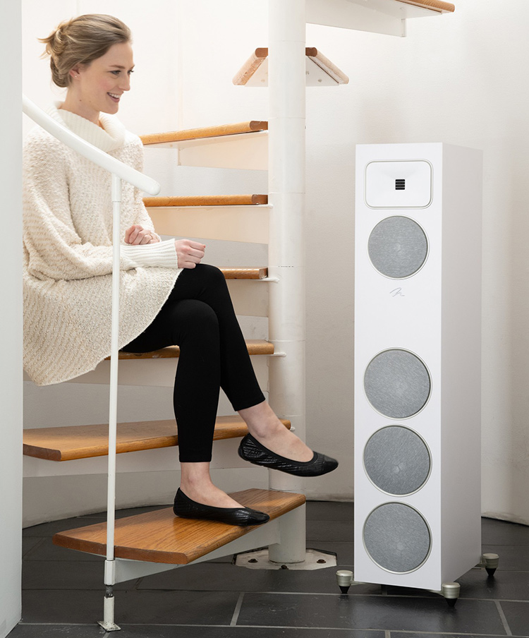 A woman sits on a staircase smiling as she glances at the MartinLogan Motion Foundation F2 Floorstanding Loudspeaker (Satin White Finish)