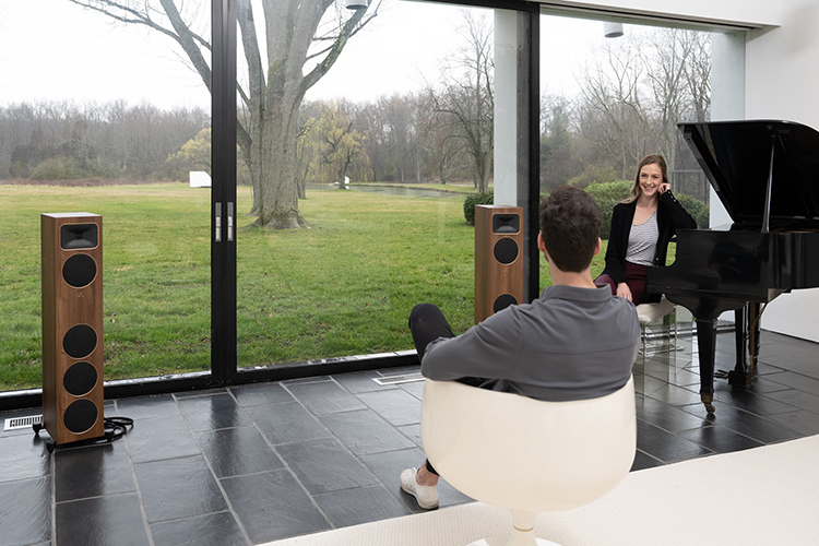 A man and a woman are sitting in a living room area nearby a window as they smile at each other with the MartinLogan Motion Foundation F1 Floorstanding Loudspeakers (Walnut Finish) situated across from them