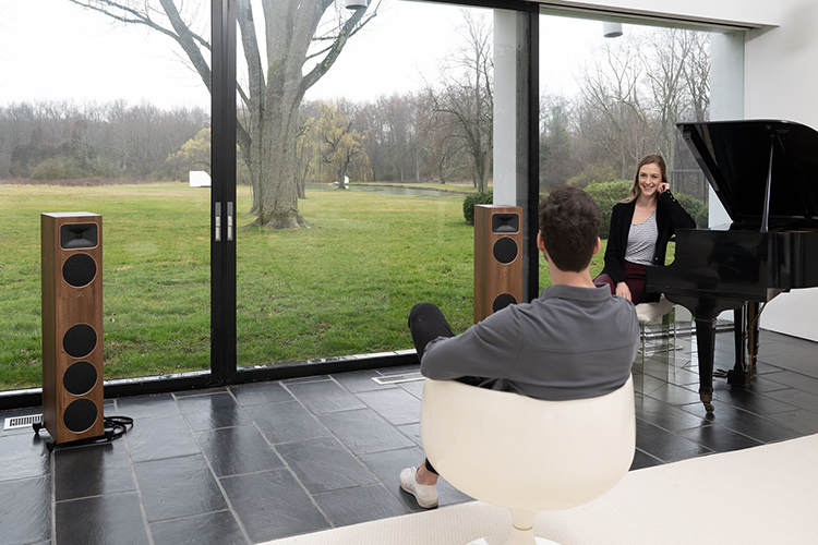A man and a woman are sitting in a living room area nearby a window as they smile at each other with the MartinLogan Motion Foundation F1 Floorstanding Loudspeakers (Walnut Finish) situated across from them