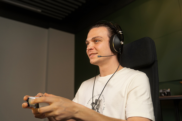 Boy smiling as he has on the Meze Audio 99 NEO Headphone with the Boom Mic while using a video game controller to play video games