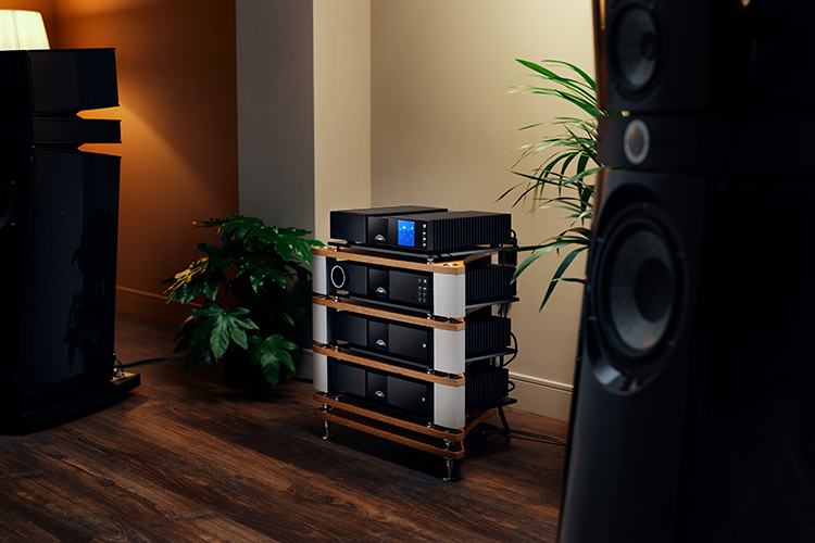 Naim Audio NSS 333 streamer, NAC 332 pre-amplifier, NAP 350 monoblock power amplifier, NVC TT phono stage and NPX TT power supply all stacked on top of each other within the living room area nearby some loudspeakers