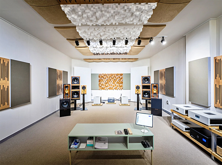 A wide-angle view of a symmetrical, professionally treated audio listening room in Seoul; The white walls are outfitted with various acoustic panels, and two large, high-end tower speakers stand prominently on the left and right, with additional equipment on low wooden racks in the center and far right