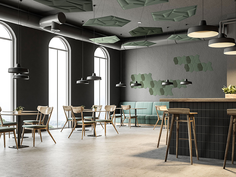 A modern, high-ceilinged cafe or common area featuring dark grey walls and large arched windows; Several light green geometric acoustic panels are suspended from the ceiling and mounted on the back wall, complementing the wood-and-green chairs and a black-paneled service counter