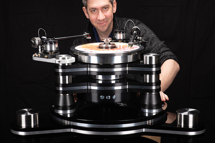 Mat Weisfeld (President at VPI Industries Inc.) stands and poses for a picture with the VPI Titan Direct Turntable as he smiles with his left arm resting on the left side bottom base of the turntable