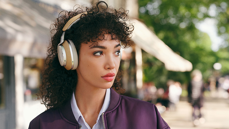 A woman listens with the Bowers and Wilkins Px8 Wireless Headphone Tan Finish on top of her head outside in town