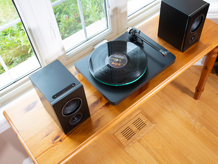 PSB Speakers Alpha iQ Streaming Powered/Wireless Bookshelf Speakers with BluOS (Satin Black Finish) on top of a table situated next to a turntable