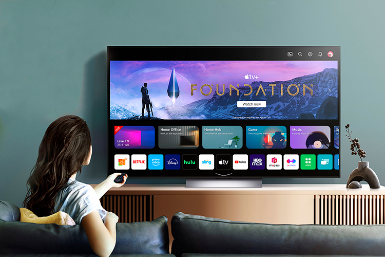 A woman uses her remote to browse the LG OLED evo TV home screen in the living room couch