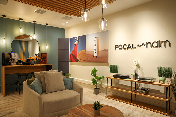 An interior landscape photograph of the Focal Powered by Naim retail space in Newport Beach featuring Focal Powered by Naim headphone displays, cases, and turntables located nearby a small sofa chair
